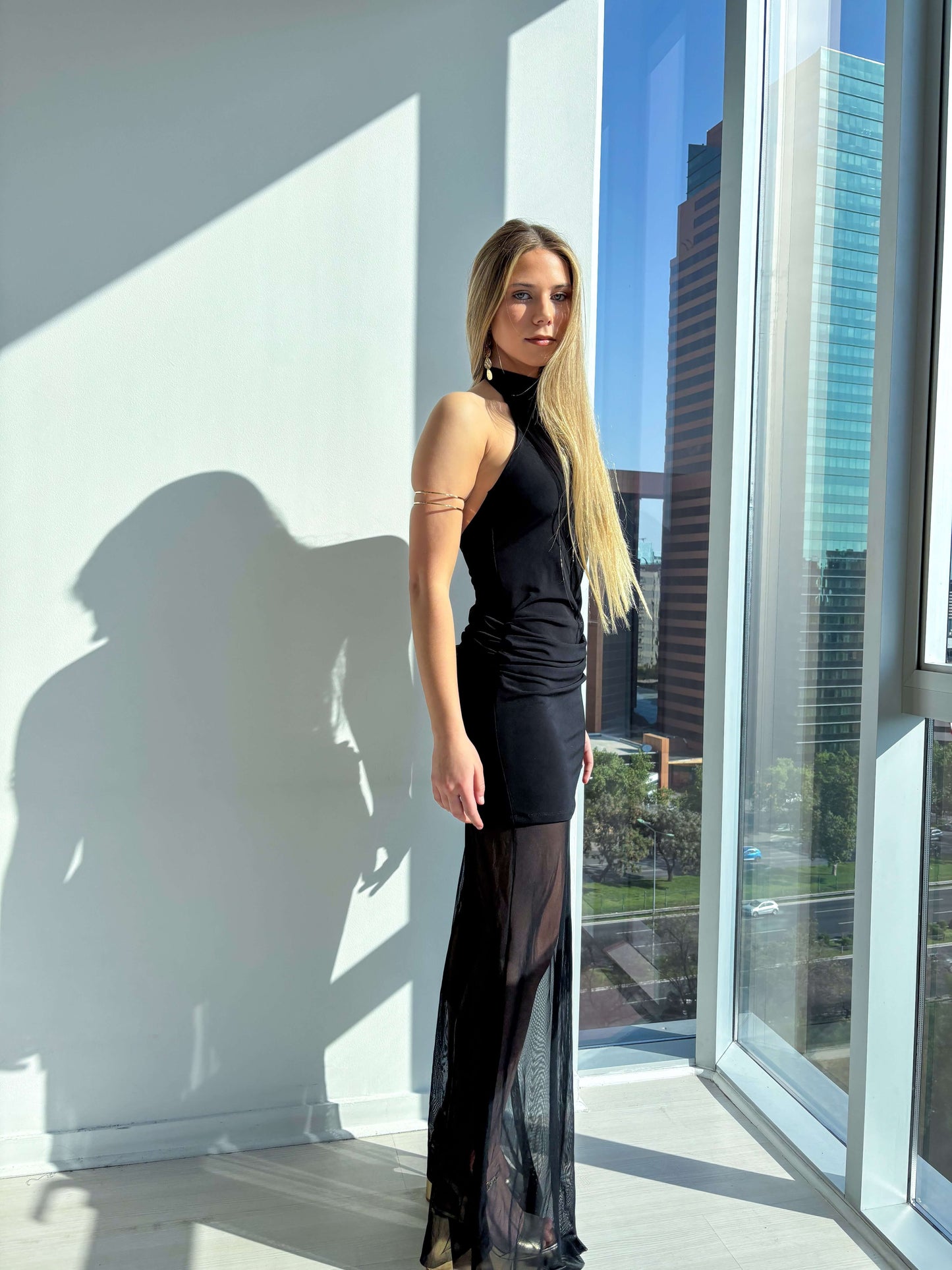 Modelo luciendo vestido elegante negro con cuello halter y falda transparente, ideal para eventos formales.