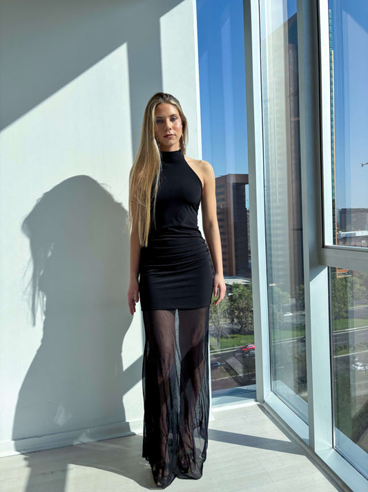 Modelo luciendo vestido elegante negro con cuello halter y falda de transparencia en ambiente moderno.