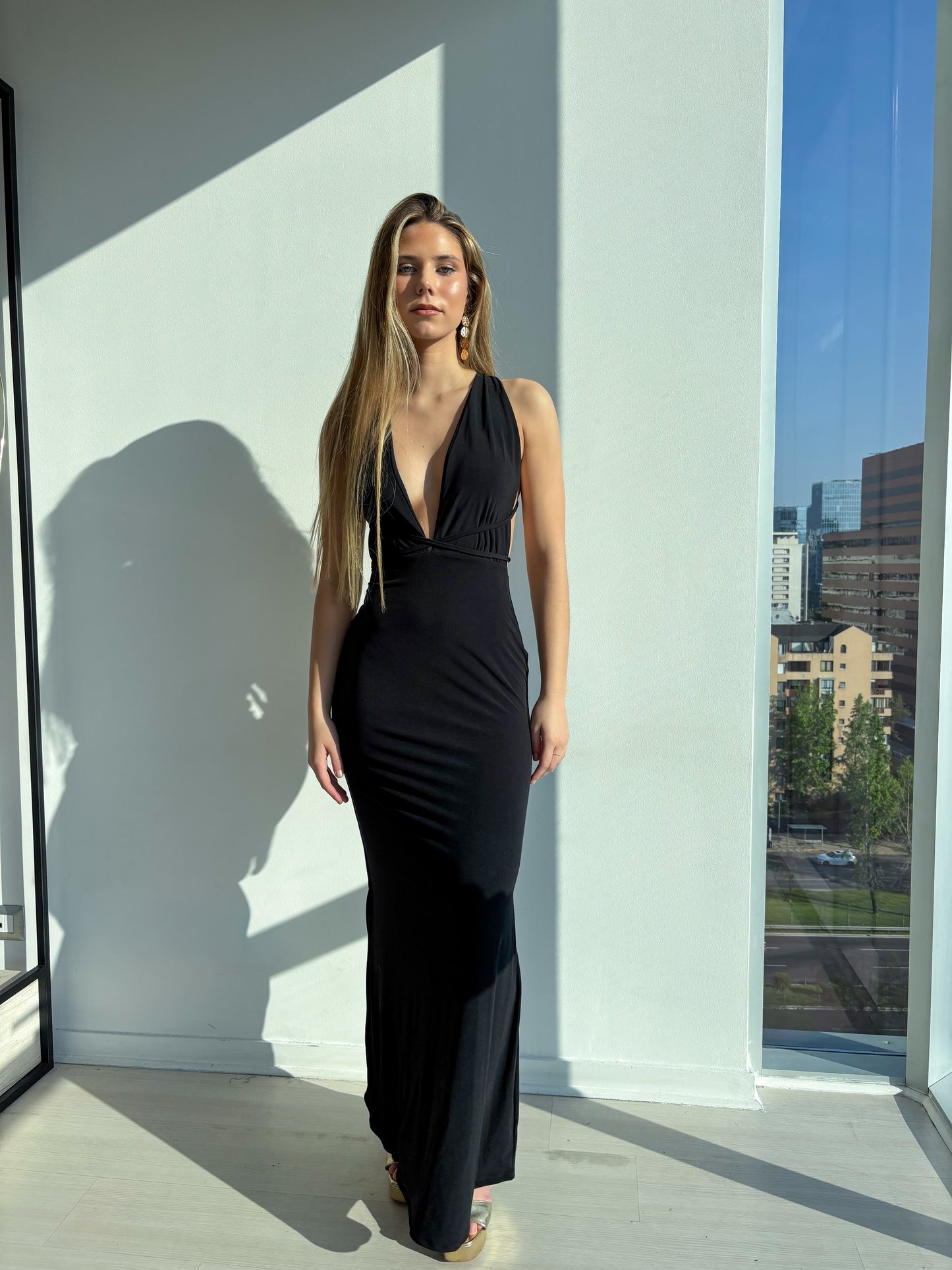 Vestido Milán Negro en una modelo frente a una ventana, elegante y ajustado, ideal para eventos formales.