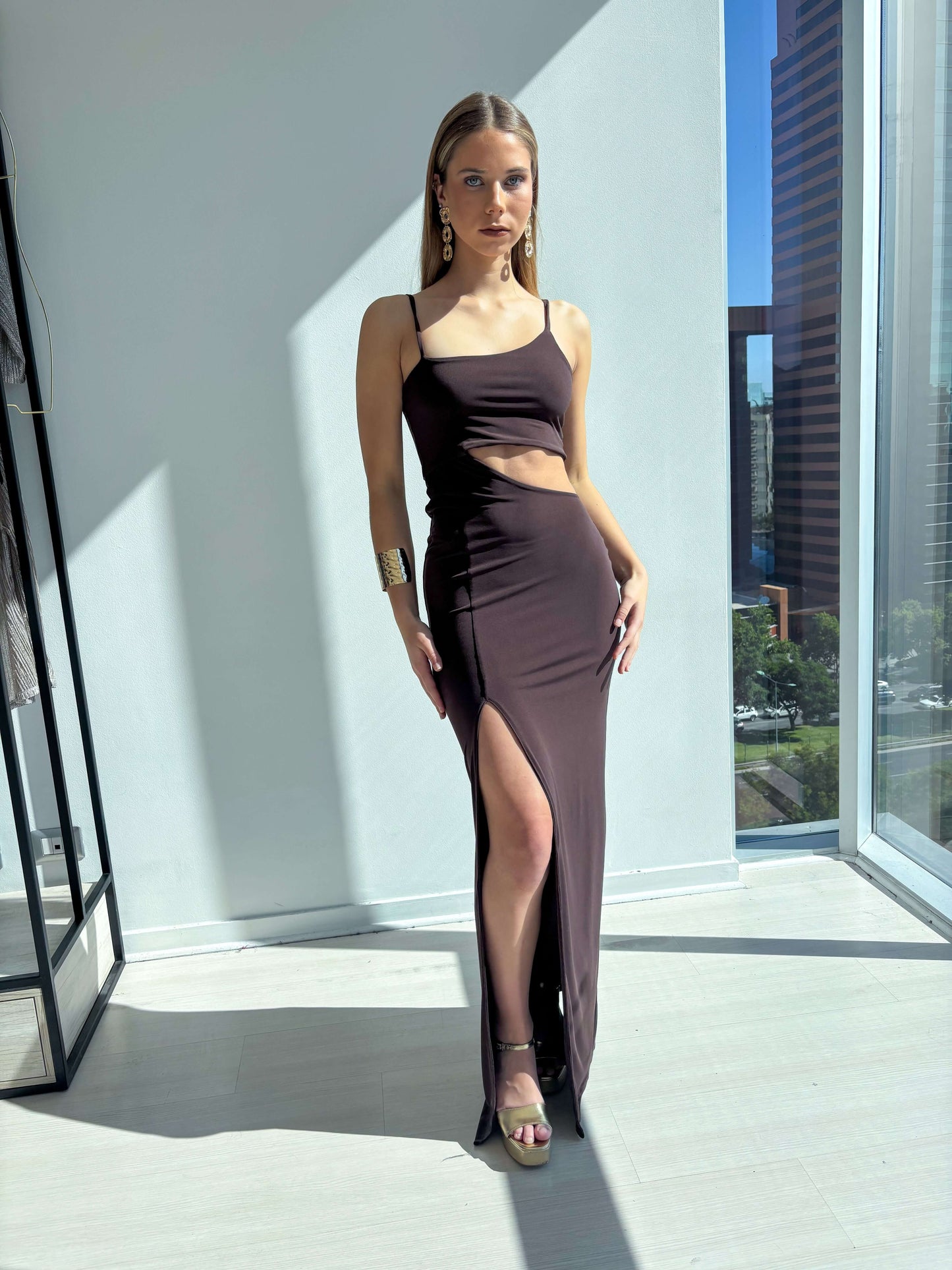 Vestido de fistes asimetrico cafe en modelo con abertura, elegante y sofisticado en ambiente moderno.