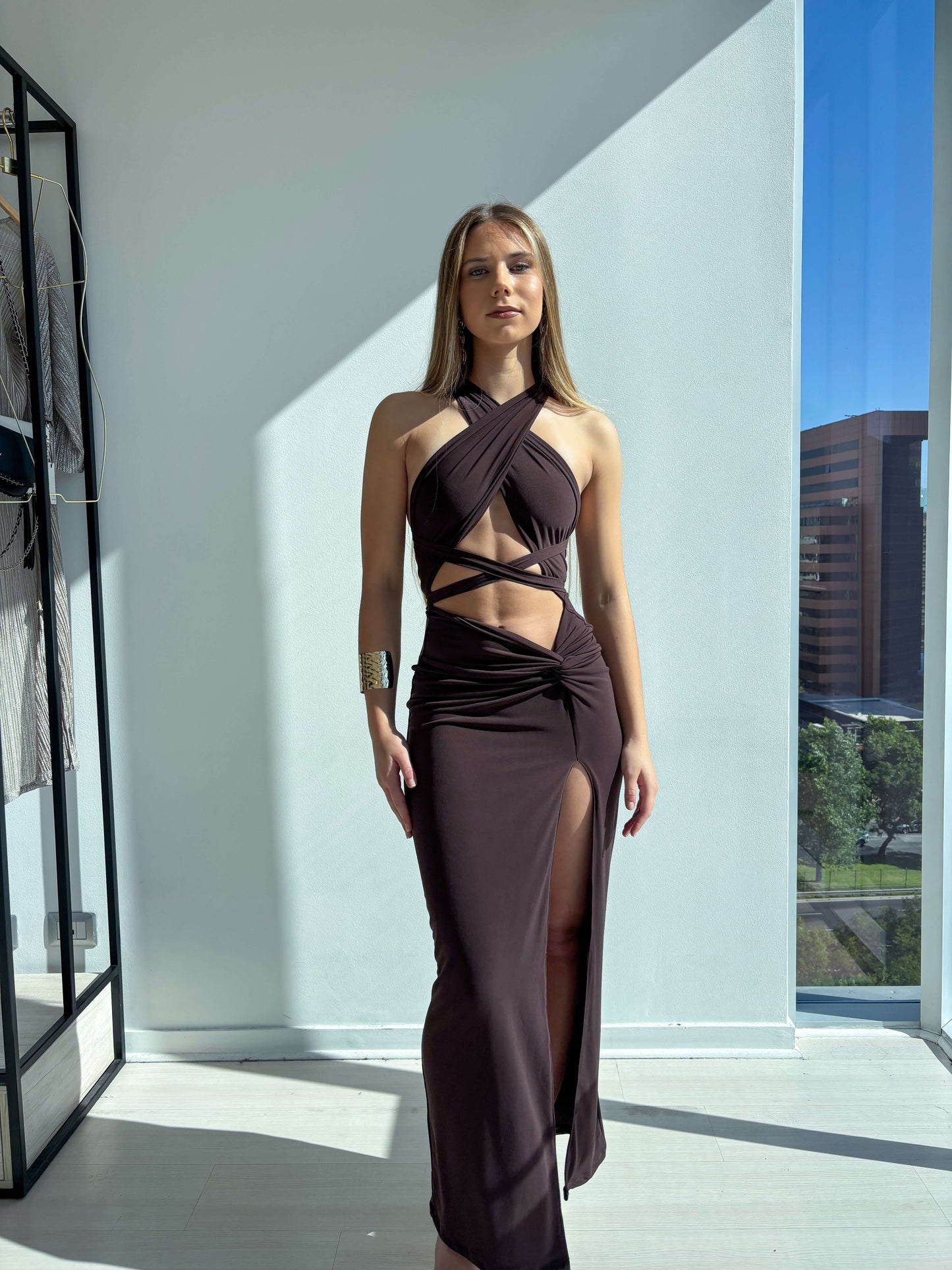Vestido Venecia Café modelo en un entorno elegante, mostrando su diseño ajustado y abertura en la pierna.
